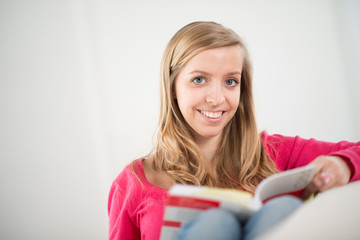 cheerful young woman reading a book on her sofa