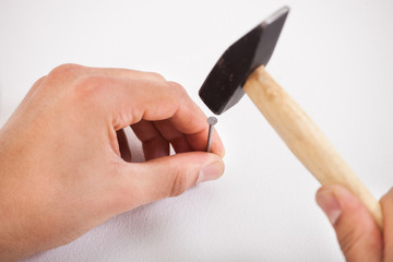 Hands hammering white wall with nail