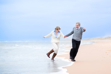 Happy middle aged couple running on a beach holding hands