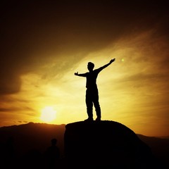 man silhouette with her hand raised in the sunset