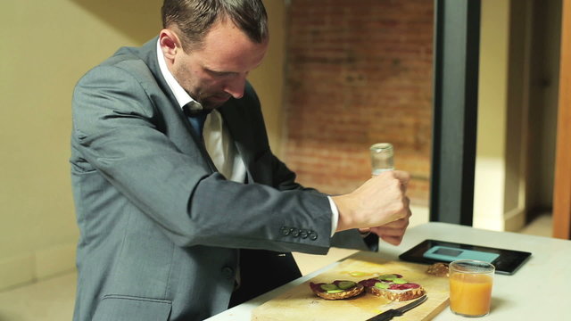 young businessman having lunch and peppering a sandwich