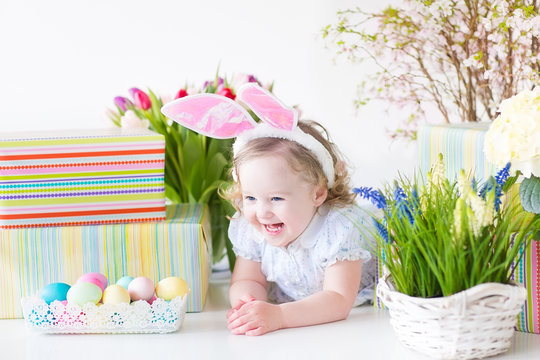 Little toddler girl with rabbit's ears next basket of eggs