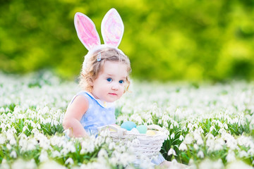 Funny toddler girl wearing bunny ears playing with Easter eggs