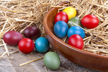 Fototapeta na wymiar Colourful Easter eggs in a wooden bowl and in the straw