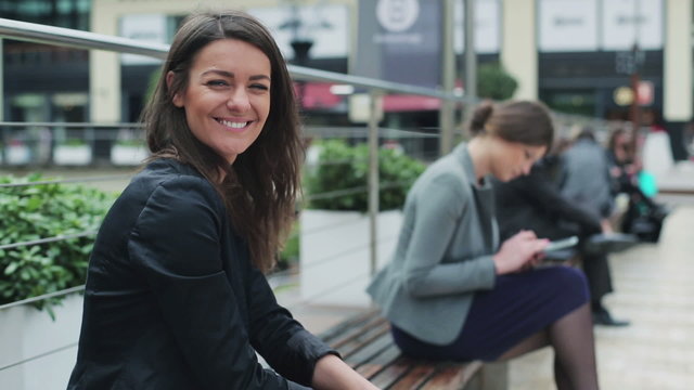 Businesswomen smiling to camera on street bench, steadycam shot