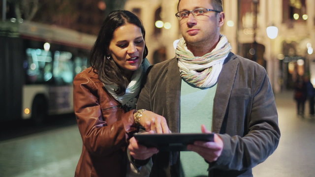 Couple checking map on tablet and walking on street at night, st
