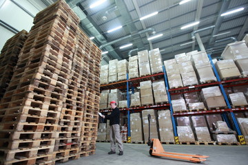worker with order at stack of wooden pallets in storehouse