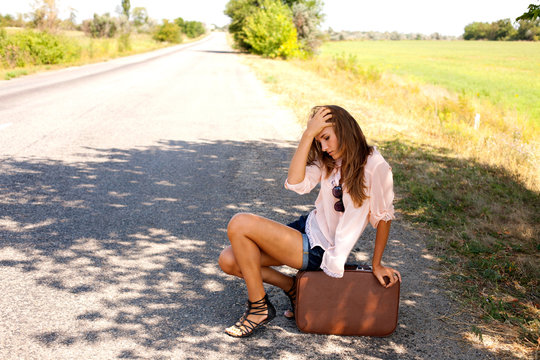 Desperate woman sitting on a suitcase by a countryside road