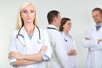 Fototapeta premium Doctor standing in front of coworkers on grey background
