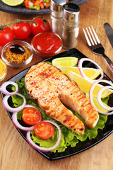 Tasty grilled salmon with lemon and vegetables, on wooden table