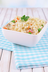 Tasty instant noodles with vegetables in bowl on table close-up