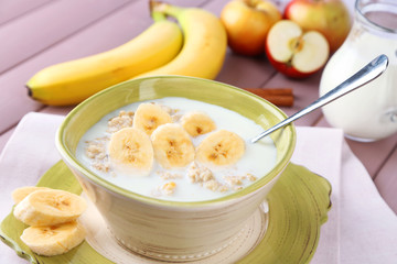 Tasty oatmeal with bananas and milk on wooden table