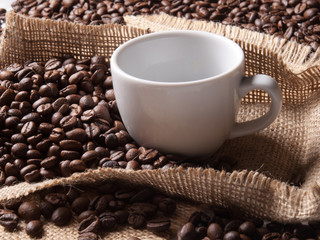 white cup with coffee on burlap background with beans