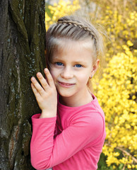little girl stands leaning against a tree