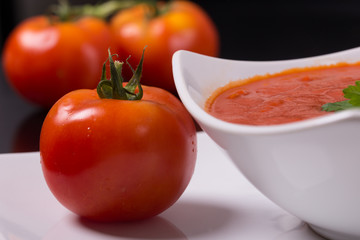 tomato soup with fresh tomatoes on black background