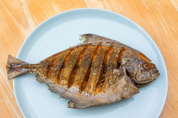 Asian style deep fried pomfret on dish in wooden table backgroun