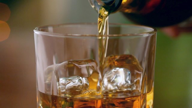 Pouring a scotch whiskey into glass with ice