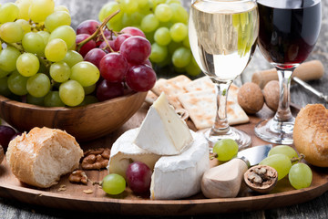 Camembert, fresh baguette, grapes and wine on a wooden tray