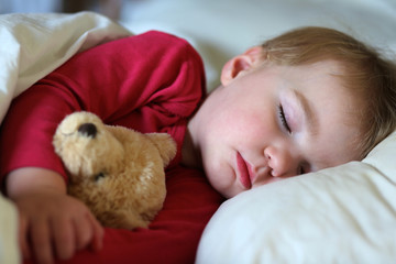 Sweet toddler girl sleeping in bed holding her teddy bear 