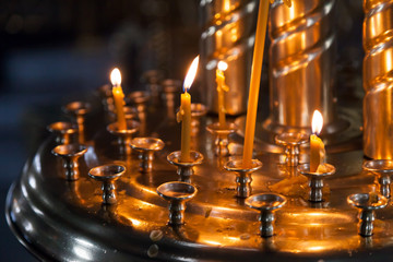 Small candles are lit in a dark Orthodox Church