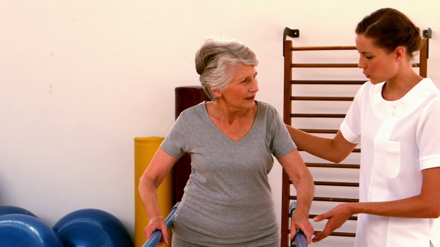 Physiotherapist helping patient walk with parallel bars