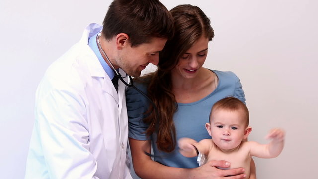 Mother holding baby while pediatrician listens to his chest
