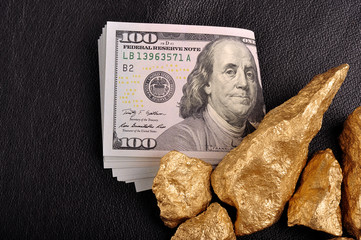 Gold nuggets and U.S. dollars on a black background leather. Clo © Andrii Medvediev