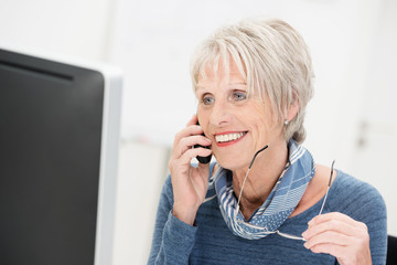 lächelnde seniorin am computer mit telefon
