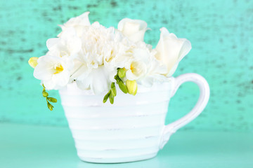 Beautiful spring flowers in cup on blue background