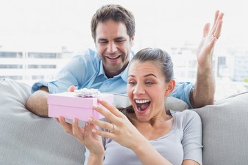 Man surprising his pretty girlfriend with a pink gift on the sof