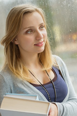 Thoughtful student holding books by window