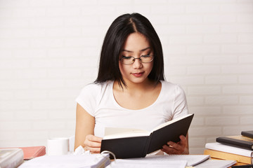 Studentin mit Brille am Schreibtisch liest Buch