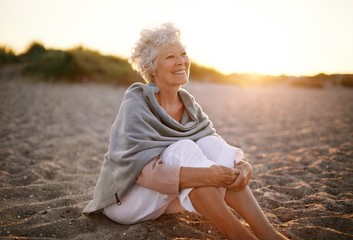 Cheerful old woman sitting on the beach - Powered by Adobe