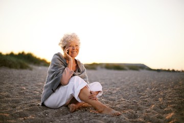 Retired woman in the beach making phone call
