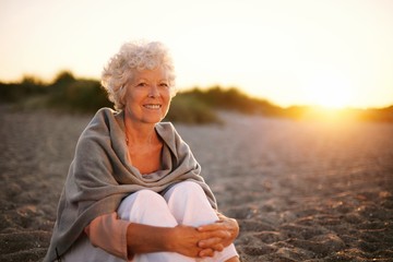 Fototapeta na wymiar Smiling old woman sitting on the beach