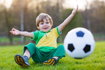 Blond boy of 4 playing soccer with football on football field