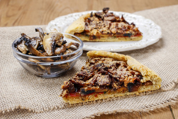 Bowl of raw mushrooms and mushroom galette in the background