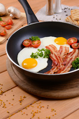 Scrambled eggs and bacon on frying pan on table close-up