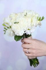 Obraz na płótnie Canvas Hand holding beautiful wedding bouquet on bright background