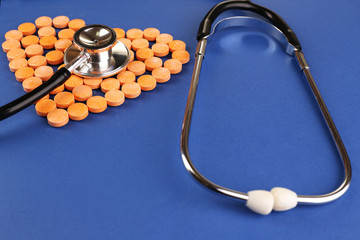 Heart of pills and stethoscope on blue background