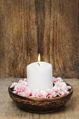 White candle among carnation flowers in vintage wooden bowl