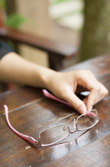 Obraz premium Pink eyeglasses in woman hand on wooden table.