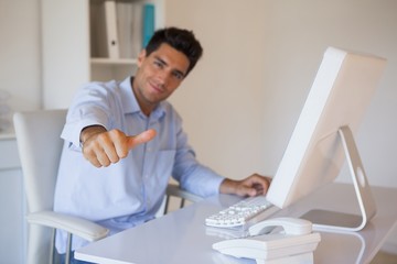 Casual businessman giving thumbs up to camera at his desk