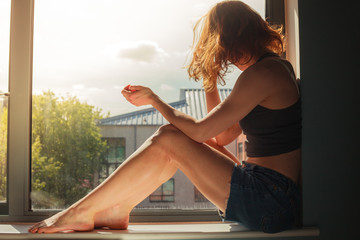 Young woman sitting on window sill on sunny day