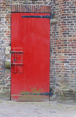 Red painted door with locks and brickwork wall