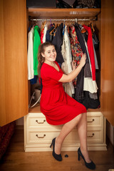 beautiful woman in red dress sitting at big wardrobe