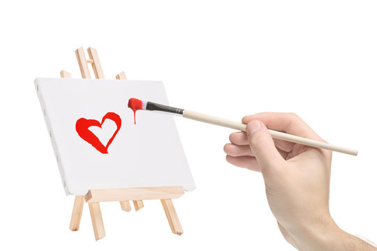 Hand with a paintbrush and a painting of a heart