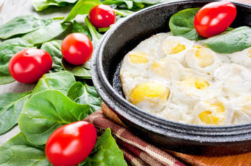 Scrambled quail eggs with spinach and tomatoes. Indoors closeup.