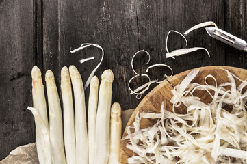 Shelled white asparagus with peelings on dark wooden table