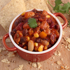 Chili con carne in red bowl with nacho chips and spice